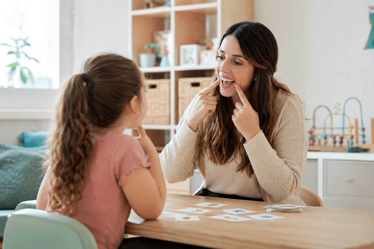 Speech-language pathologist guiding a child through speech sounds at a therapy table.