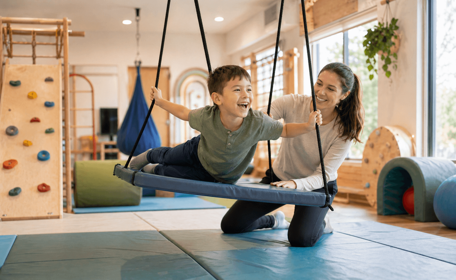 Child exploring a sensory gym for autism and sensory processing disorder with a pediatric occupational therapist nearby, featuring swings, climbing equipment, and proprioceptive play structures
